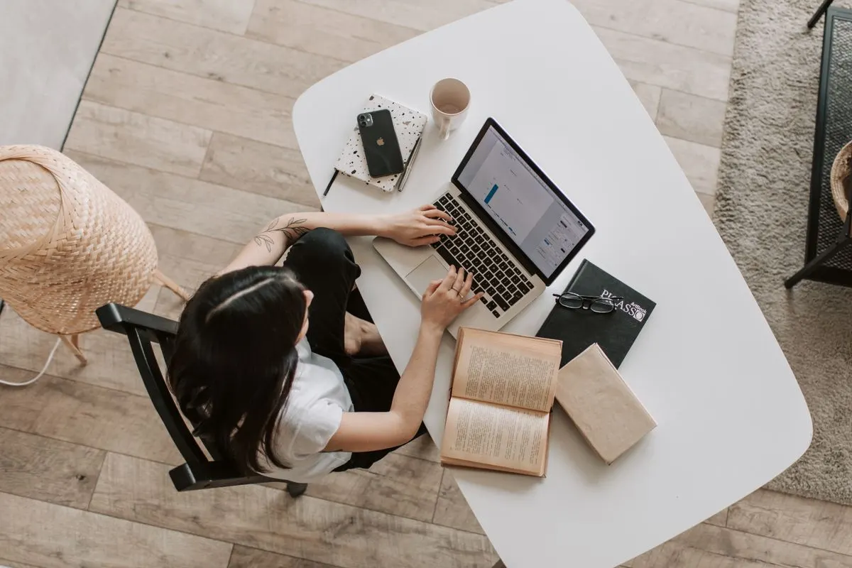 A desk with tablet displaying blockchain, laptop, book, and camera lens, symbolizing tech and…