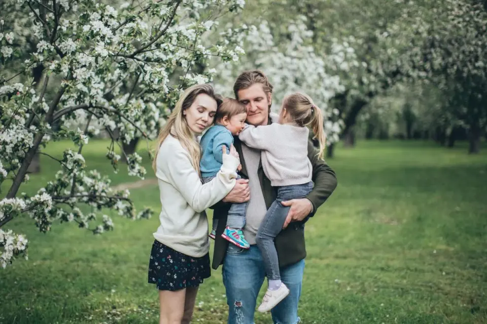 Milující rodina se objímá pod rozkvetlými stromy v pulzujícím jarním parku. - Foto: Elina…