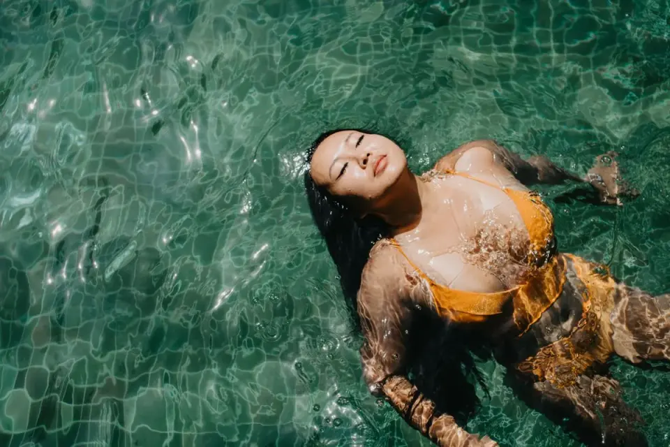 Asian woman in a yellow bikini enjoying a peaceful swim in clear waters. - Photo by Anna…