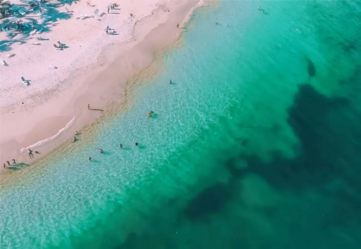 Stunning aerial shot of a tropical beach with clear turquoise waters and sunbathing people. -…