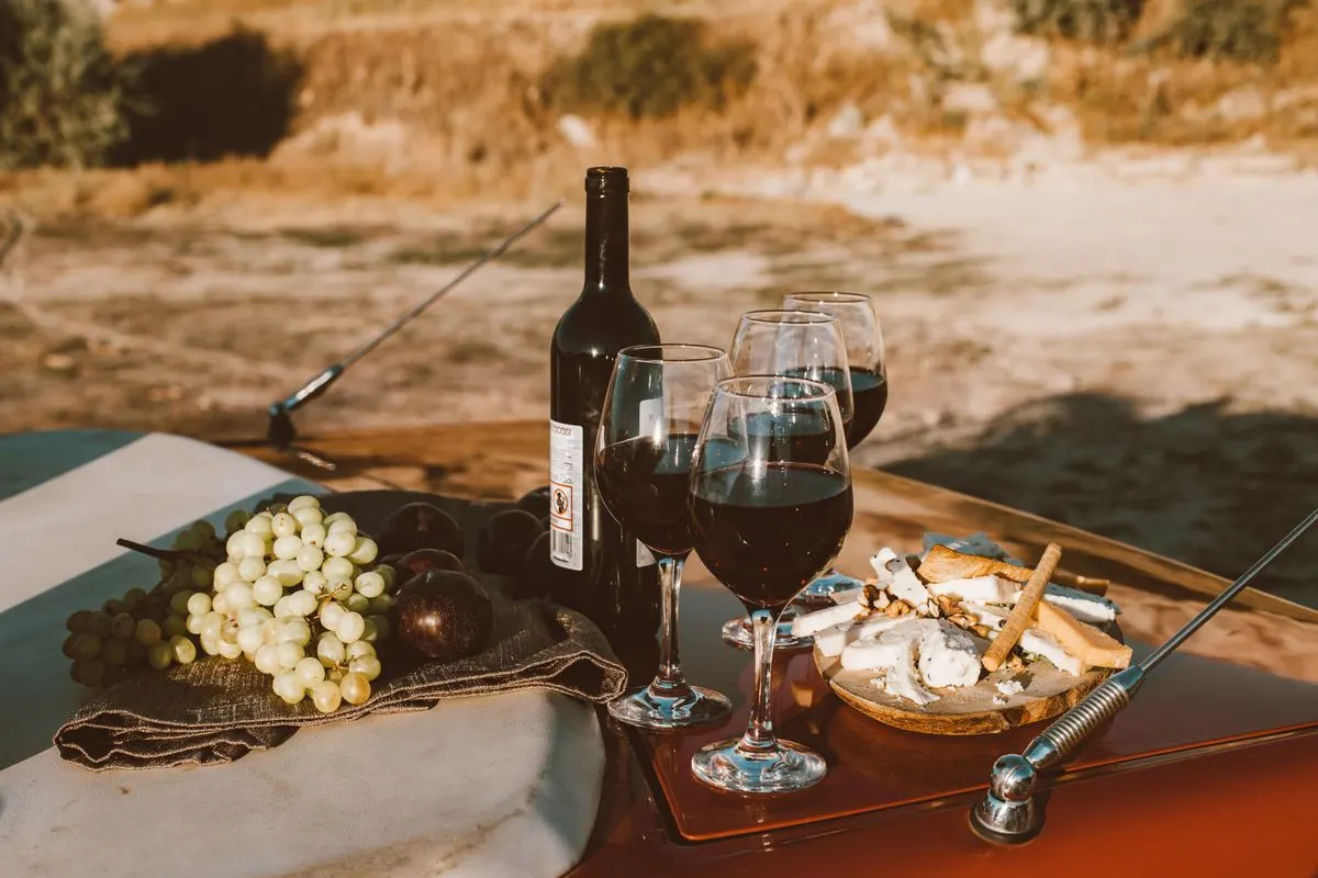 A rustic outdoor picnic setup featuring wine, grapes, and cheese on a car bonnet. - Photo by…