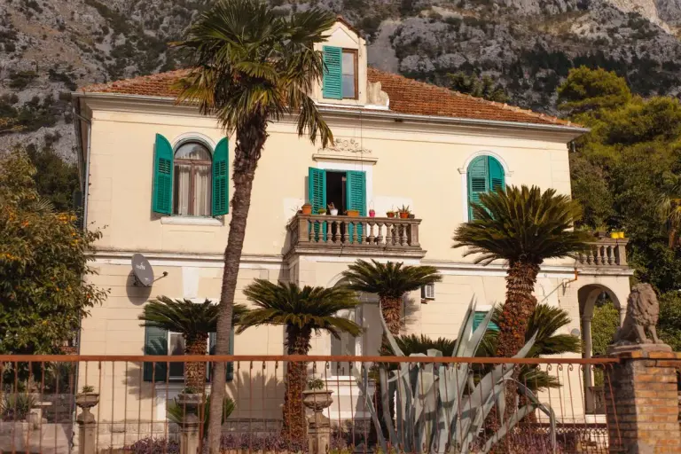 Beautiful Mediterranean villa with vibrant shutters, surrounded by palm trees in a mountainous…