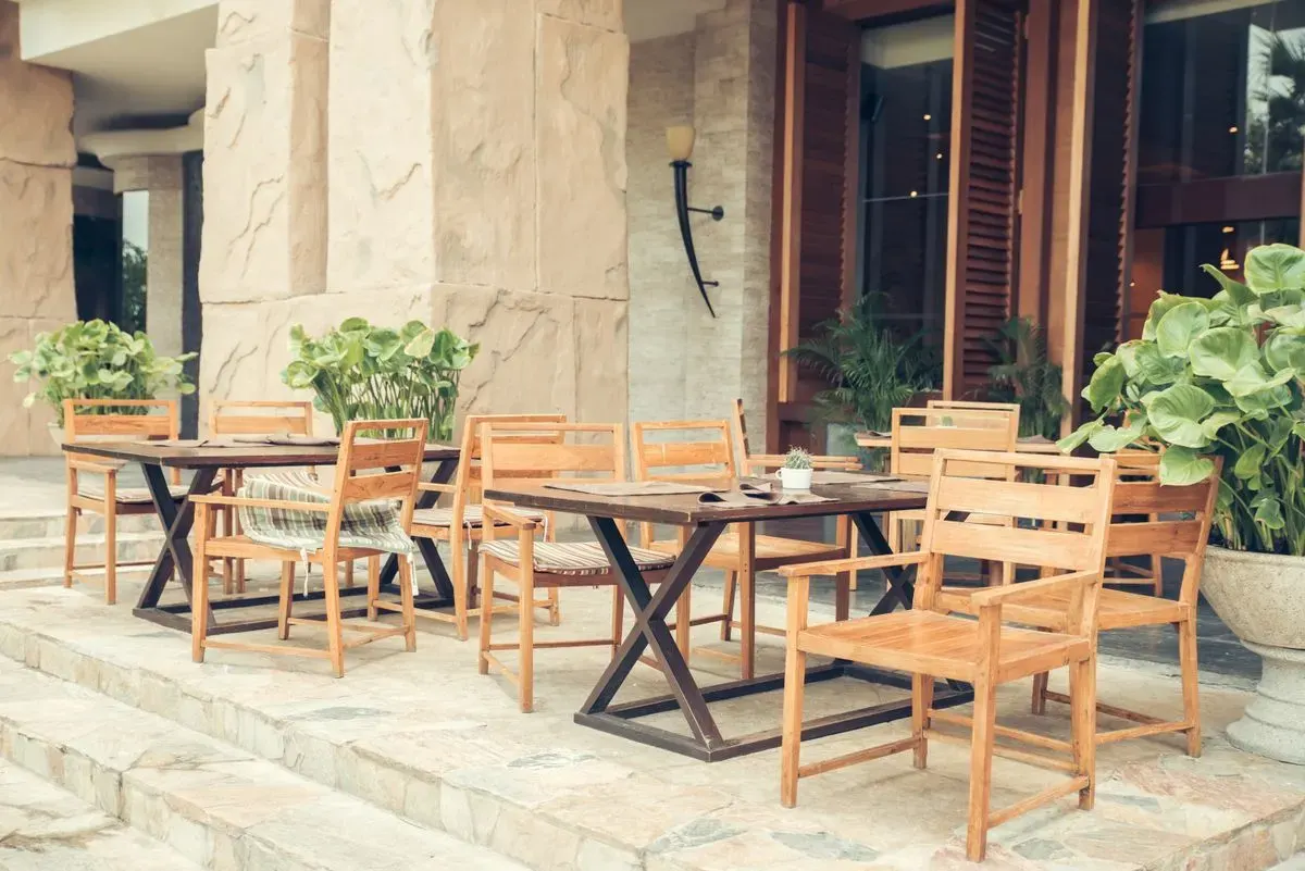 Elegant outdoor café area with wooden chairs and tables, decorated with lush greenery. - Photo…
