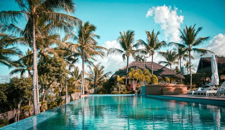 Scenic view of a luxury tropical resort with palm trees and an inviting pool. - Photo by Cesan…