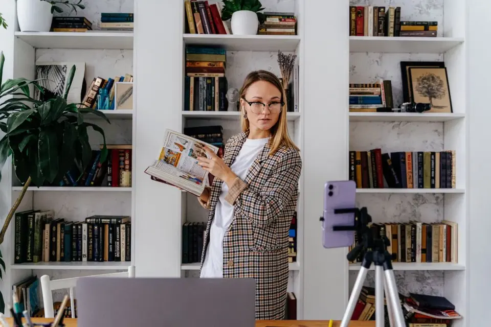 A woman recording a vlog in her home library, using a smartphone and tripod setup. - Photo by…