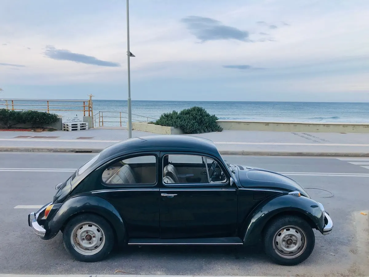 Classic Volkswagen Beetle parked by the Aegean Sea in Rethymno, Greece, under a cloudy sky. -…