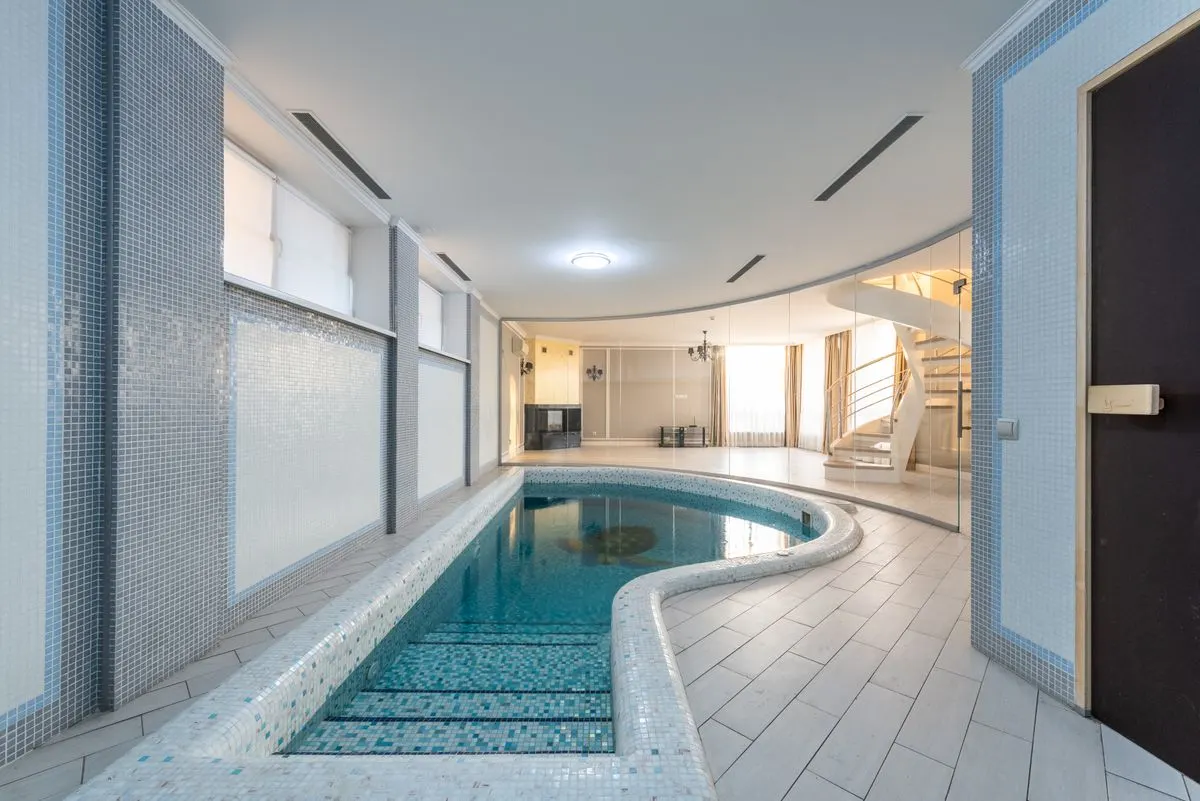 Serene indoor pool area with modern design and spiral staircase. - Photo by Max Vakhtbovycn on…