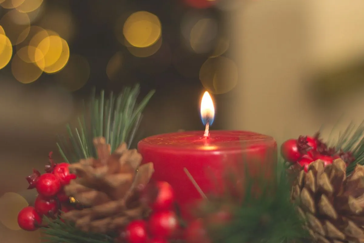 Red candle with pine cones and blurred bokeh lights, perfect for holiday decor inspiration. -…