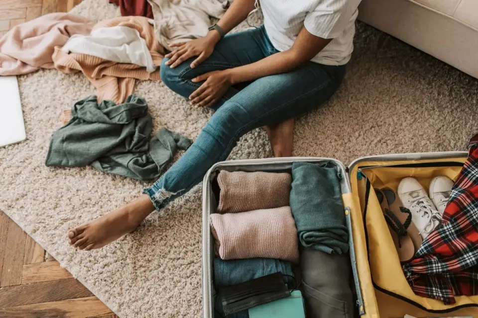 Woman organizing clothes while sitting on floor with open suitcase, preparing for a trip. -…
