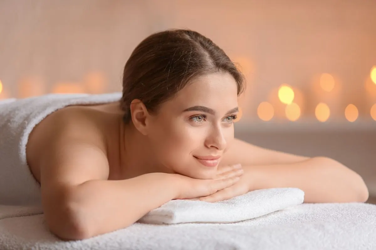 A serene woman enjoying a spa experience with flickering candles, wrapped in a towel, portraying…