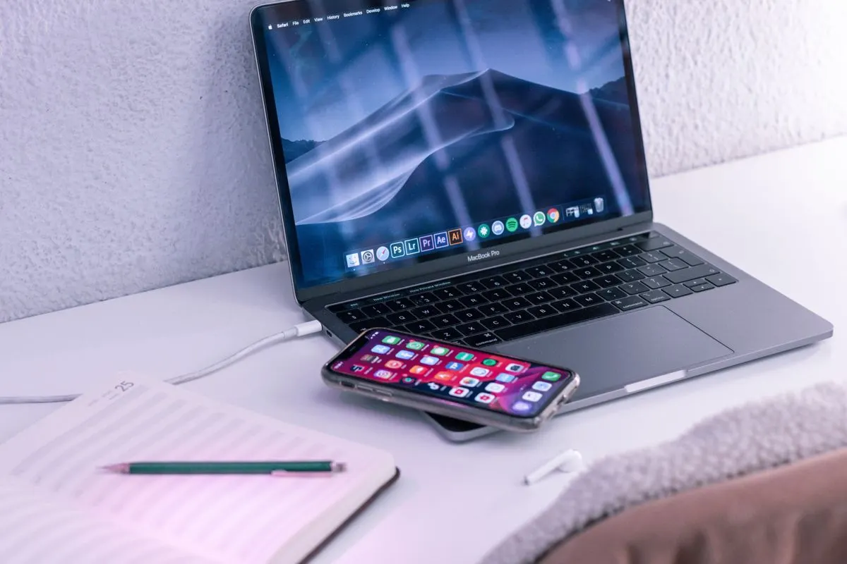 High angle of opened netbook with mobile phone placed near notepad and wireless earbuds for…