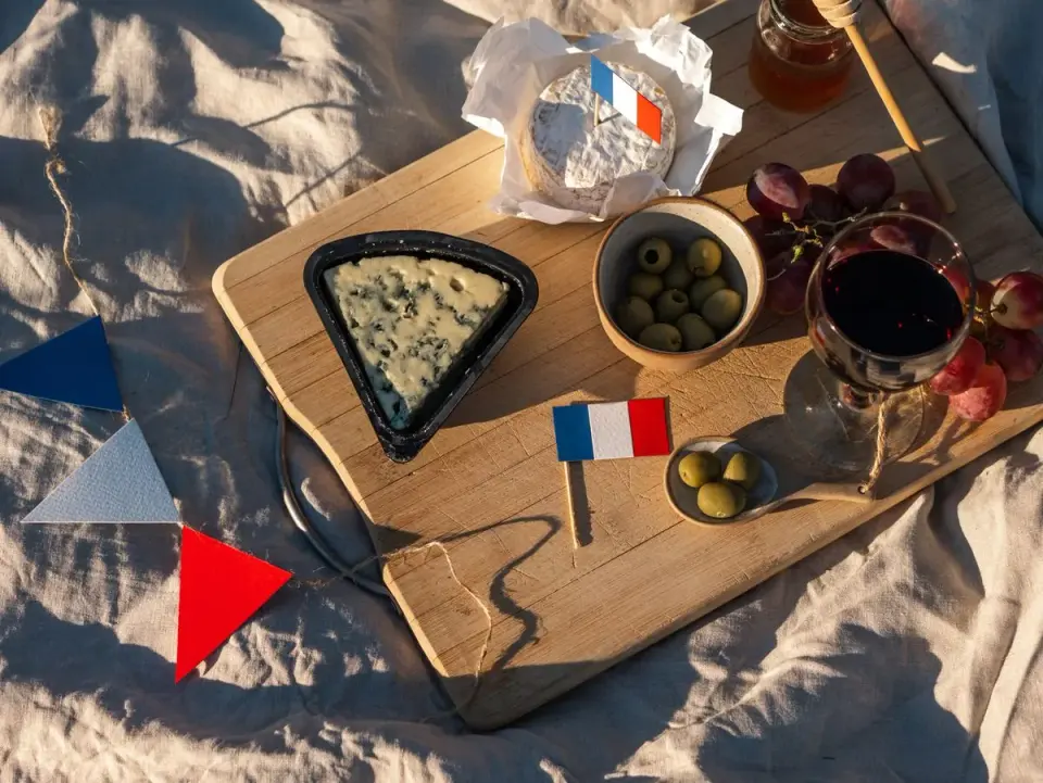 A rustic French picnic with wine, grapes, cheese, and a flag arranged on a wooden board. - Photo…