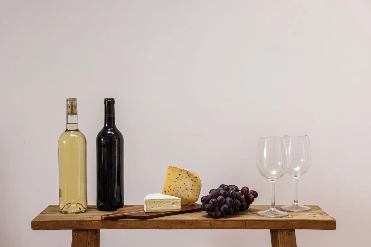 A rustic setting with wine, cheese, grapes, and wine glasses on a wooden table. - Photo by Cup…