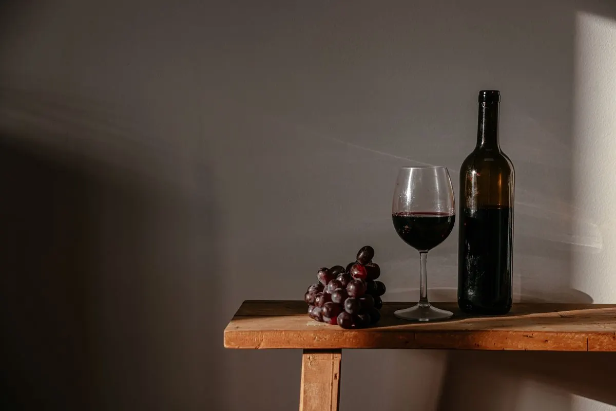 Sophisticated still life featuring red wine, a bottle, and grapes on a rustic wooden surface. -…