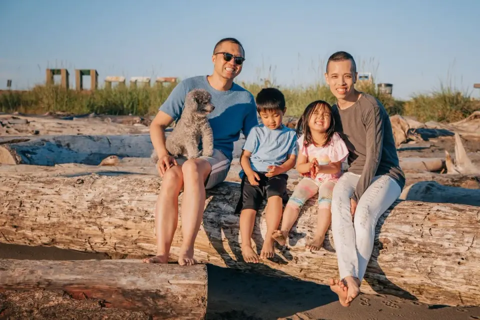 Family with kids and a dog enjoying a sunny day at the beach, sitting on logs. - Photo by PNW…