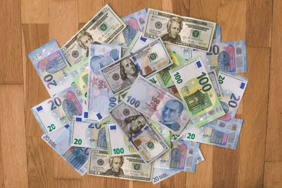 A collection of US dollars, euros, and Turkish lira banknotes on a wooden surface. - Photo by…