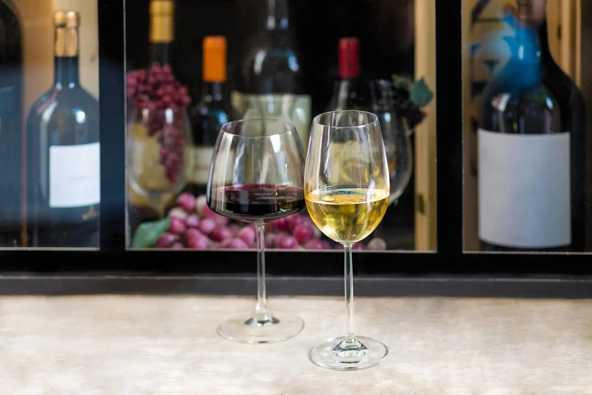 Close-up of red and white wine glasses with bottles and grapes in the background, perfect for…