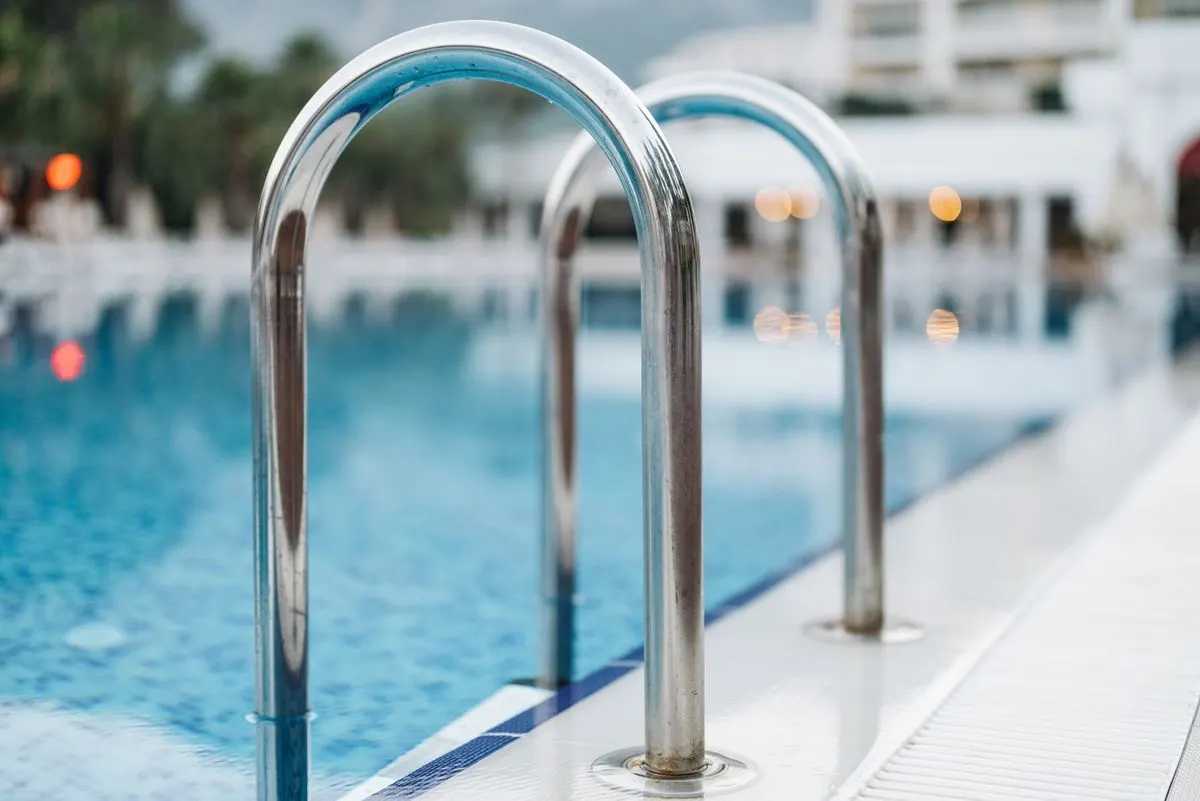 Close-up of a pool ladder at a serene resort, evoking summer vacation vibes. - Photo by Pavel…