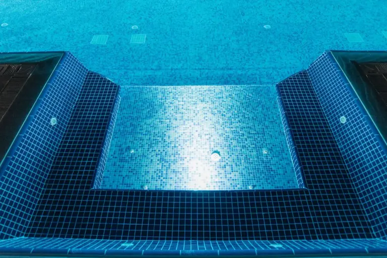 A clear view of an illuminated swimming pool with blue mosaic tiles, perfect for summer…