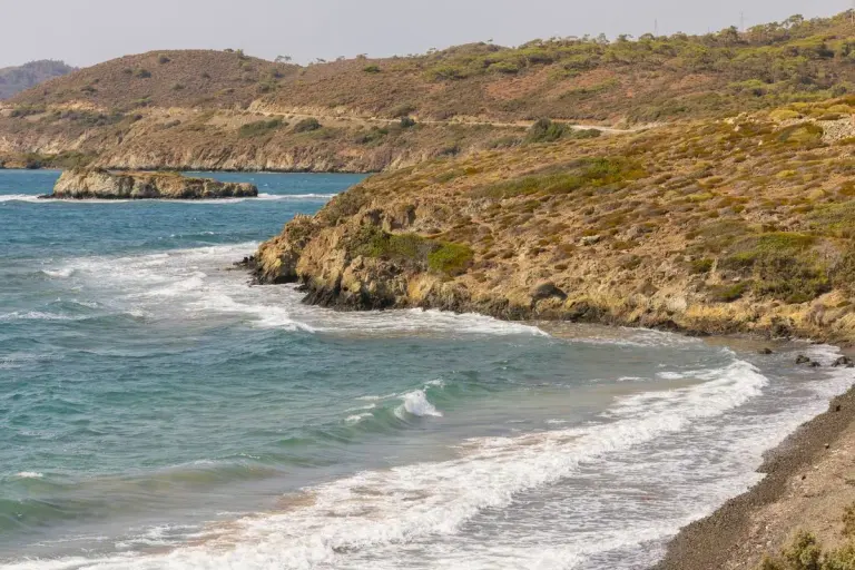 Dramatic coastal scene with waves hitting rugged cliffs against a backdrop of clear blue water.…