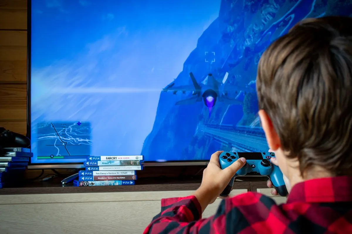 Young boy playing video game on TV with PS4 controller, enjoying leisure time indoors. - Photo…