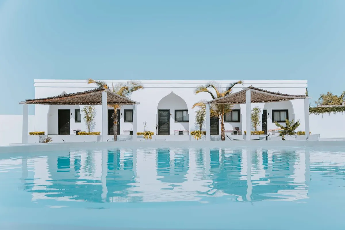 Elegant white villa in Zanzibar featuring a stunning swimming pool and palm trees under a blue…