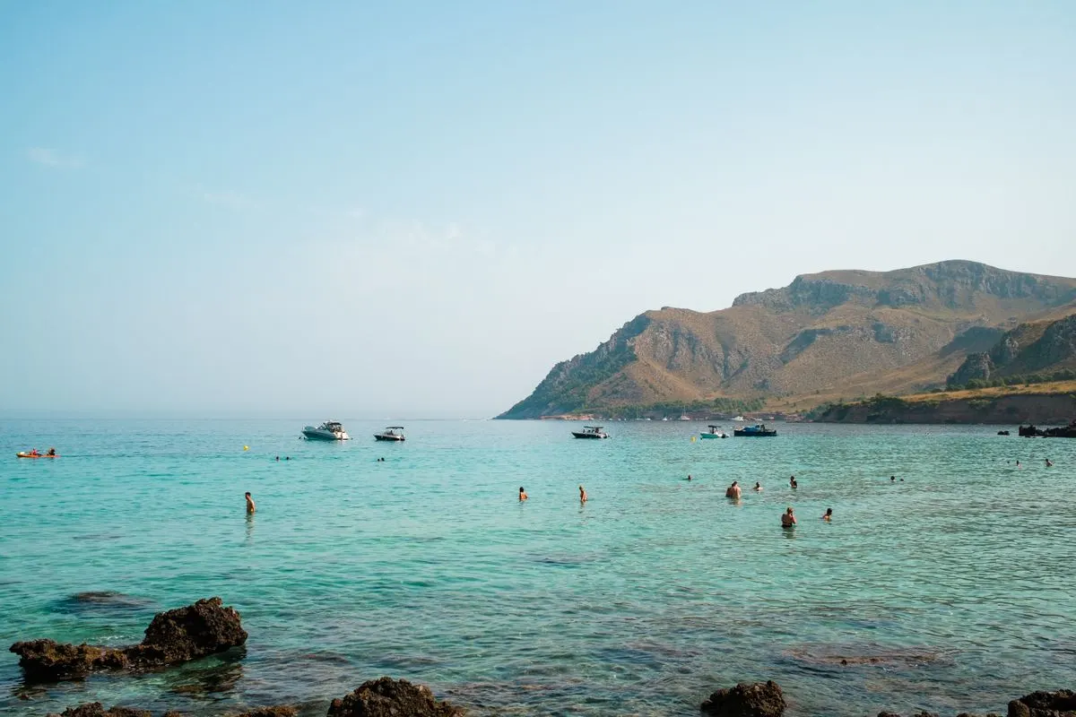 A beautiful coastal scene with clear waters, boats, and swimmers on a sunny day. - Photo by…
